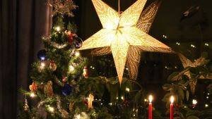 I år kommer många av oss att sköta en större del av julinköpen än vanligt hemma i soffan. Arkivbild. Julstjärna i fönster, julgran, två röda stearinljus och ett skrivbord. Stämningsbild. Skymning.