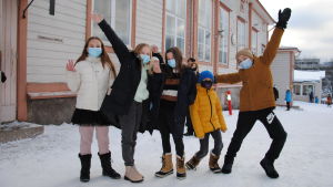 Trots allt verkar eleverna ändå ta munsskyddsbärandet med ro. Fem barn med munskydd står på snöig skolgård och poserar för kameran med händerna i luften.