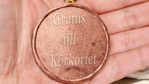 Hur lång tid det tar att lära sig köra är individuellt, säger examensmottagare Johan Hindrén, som har klarat sig helskinnad genom många körprov. en medalj i brons där det står "grattis till körkortet".