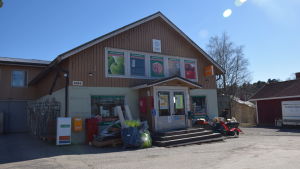 I bybutiken i Bromarv finns det just nu fullt av nyanlända varor som ska stuvas in i alla tänkbara hyllor och vrår i väntan på den livliga sommarkommersen. För ägarna är det däremot väldigt viktigt att butiken finns till för Bromarvborna året runt. I dagens läge är butiken också en bra arbetsgivare. En butik i Bromarv, fotograferat utifrån. Vår och soligt.