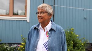 Anneli Honkanen har bott i Kuppis nästan hela sitt liv. En äldre kvinna står framför ett ljusblått hus.