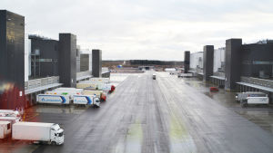 Vy från ett fönster i mitten av den u-formade byggnaden. Nere på marken syns många av de hundratals lastningsterminalerna där bilar kan lasta på och av varor. Vy från ett fönster i mitten av en u-formad byggnad. U:ets armar synns till vänster och höger. De har öppningar där lastbilar har backat in för att lasta av varor. Området i mitten är ett stort öppet område med asfalt.