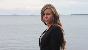 Erica Helin säger att sådana här förändringar påverkar hela samhället i Nagu. Erica Helin tittat allvarsamt i kameran. Svart klädsel, havet i bakgrunden.