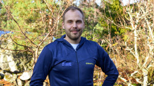 Martin Norrgård. En man med skägg står i solen och ler. Han har en blå jacka med svenska landslagets tryck på.