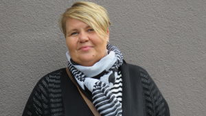 Fredrika Lindqvist, eller Fia som hon kallas, har lång arbetserfarenhet från Kårkulla. Hon har också varit verksam inom FDUV. De senaste åren har hon jobbat på eftiset Delfinen. En kvinna med kort blont hår och mörka kläder. Ler lite och ser in i kameran. Gråbrun, rappad stenfasad i bakgrunden.