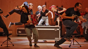 Tolvmannaensemblen dansar, sjunger och spelar i välsmorda och snygga koreografier. I förgrunden Ulriikka Heikinheimo och Robert Kock. Bakom dem Alexander Wendelin, Pia Runnakko, Vilja Seivo, Santeri Helinheimo-Mäntylä och Aili Järvelä. Scen ur föreställningen "Once" på Lilla teatern i Helsingfors hösten 2020.