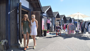 Christelle och Cecilia Rewell har börjat plocka ihop när sommarsäsongen börjar vara över. Två unga kvinnor i solglasögon och klänning står bredvid en butik som finns i en stuga. I bakgrunden finns flera likadana blåa stugor och en del kläder som hänger på stänger.