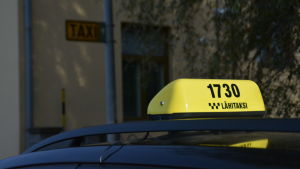 Lenita Lindholm fortsätter trots allt att köra taxi. En gul taxiskylt på en taxibil.