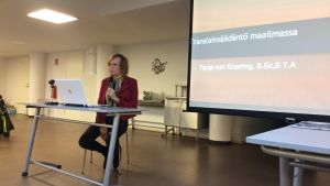 Tanja von Knorring håller en föreläsning med mikrofon i handen och framför en dator.