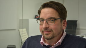 Thomas Grandell säger att det är billigare att kontakta en chattläkare via en app än att besöka en privat läkarstation. Thomas Grandell, en man med glasögon, kort skägg och mustasch, och en rosa piketskjorta under en blå tröja.