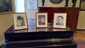 Bröderna Berthold t.v. och Claus von Stauffenberg. Fotografier står på ett piano. De föreställer bröderna Berthold t.v. och Claus von Stauffenberg t.h.