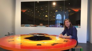 Jan-Erik Andersson har arbetat med bord eftersom han känner att de påverkar människans möjlighet att kommunicera. Här sitter han vid "Filosofens bord". Konstnär sitter vid ett stort orange bord.