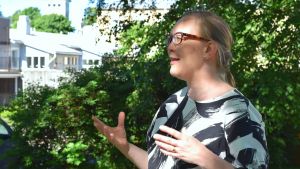 Katja Långvik är med och arrangerar konstläger för barn. Katja Långvik i profil medan hon talar och ler. Hon är utomhus med ett träd och en byggnad i bakgrunden en varm sommardag i Ekenäs.