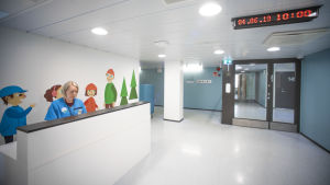 Byggnaden var förut en hälsostation. Staden har renoverat den för 4,9 miljoner euro, så att den ska lämpa sig för familjetjänster. En korridor med en disk. Bakom disken sitter en kvinna med hälsocentralskläder.
