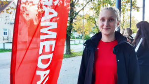Malin Sjöblom har fått många nya vänner via handbollen. Ung kvinna bredvid en röd "gameday" flagga.