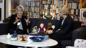 I dag skulle nog inte Elisabeth skriva så våldsamma romaner som hon gjorde när hon var barn. Elisabeth Rehn och Christoffer Strandberg sitter på en soffa. Christoffer är utklädd till Elisabeth i kavaj, peruk och pärlhalsband.