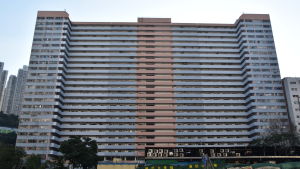 Gigantiska före detta industribyggnader inhyser nuförtiden också ateljéer. Hyrorna är inte lika skyhöga som i andra byggnader. En bild på ett höghus i Hongkong. Huset är blått och orange. Det står gröna träd framför det.