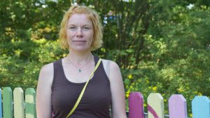 Jenni Kainulainen har tidigare jobbat på kommunala daghem. Under sin föräldraledighet för sju år sedan blev hon företagare när hon och hennes man startade daghemmet i Ingå. En kvinna med rött lockigt hår i brunt linne. I bakgrunden syns grön skog och ett staket.
