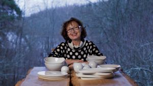 Karin Widnäs öppnade museet i år. Kvinna med mörkt lockigt hår och glasögon sitter vid bord med keramik och ler.