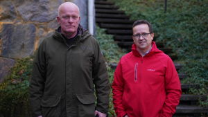 Jörgen Engroos till vänster och Johan Ljungqvist träffades för första gången i samband med en guidad rundtur i bunkern Irma. Efter det har de träffats många gånger. Två män står ute, ser in kameran. BAkom en trappa och vintergröna, marktäckande växter.