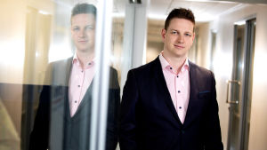 André Heikius säger att det finns många duktiga och empatiska läkare men att det inte alltid blir så att patienterna får ett bemötande där de känner sig bekväma. Man med svart kavaj, brunt hår och ljusrosa skjorta. Står lutad mot en glasvägg i vilken han reflekteras.