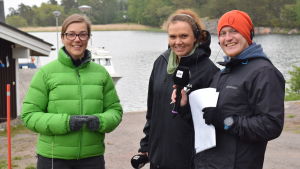 Forskningskoordinator, tf direktör Joanna Norkko med redaktörerna Veronica Montén och Sebastian Dahlström under Yle Västnylands direktsändning från Tvärminne zoologiska station. En kvinna i grön, ganska varm rock intervjuas av en annan kvinna och en man. Radiointervju. I bakgrunden en brygg, båt och vatten plus ett hus vid bryggan.