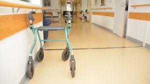En rollator på bädden i Hangö som bara väntar på att bli använd. En rollator i korridoren på en bäddavdelning.