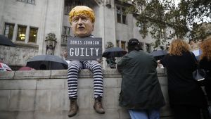 En demonstrant sitter utanför Högsta domstolen i London. På skylten står det "Boris Johnson skyldig". En demonstrant i fångdräkt och en Boris Johnson-mask sitter utanför Högsta domstolen i London.