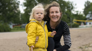 Eva Länsiluoto får bita ihop och klaga vill hon inte. En kvinna och ett litet barn i gul jacka som tittar mot havet.