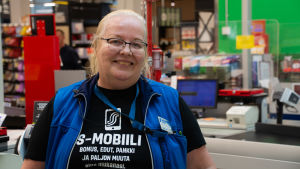 Marianne Bäckman har läst om de senaste händelserna i Nickby bland annat på sociala medier. Marianne Bäckman står vid kassan och ler.