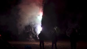 De offentliga fyrverkerierna var mestadels inhiberade, men många privatpersoner firade med egna fyrverkerier. Bilden är från stadsdelen Drumsö i Helsingfors. Siluetten av två personer syns framför en rykande fyrverkeripjäs.