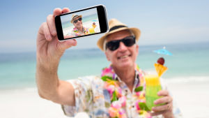 Nästan perfekt, Berra! Men ta av solbrillorna ännu! Leende äldre man tar selfie på strand