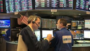 Börsen på Wall Street kan ha betydelse också för finländarna. Två aktiemäklare vid dagens slut, med stora datorskärmar som visar kurshändelser+Donald Trump på TV.