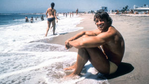 Arnold Schwarzenegger istuu uimarannalla 1970-luvulla.