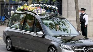 Lyra McKees kista körs till kyrkan. Bil med blommor på taket kör till begravning.