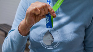 Arja Palmu visar upp sin VM-medalj. Då hon för 20 år sedan tog medalj i FM så var den helt av metall. Hand håller upp silvermedalj