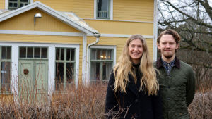 Ida Söderström och Oscar Gräsbeck lämnade storstaden för Bromarv för att ge gården nytt liv. Ida Söderström och Oscar Gräsbäck står utomhus framför ett gult gammalt trähus.
