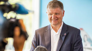 Norwegians koncernchef Jacob Schram säger att regeringens beslut är orättvist. Norwegians koncernchef Jacob Schrem talar i en fluffig mikrofon och ler mot en kamera.