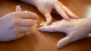En vardagsaktivitet kan vara att göra naglarna fina på en äldre som bor hemma, men kanske har svårt att själv få det gjort. Bild på två par händer. Den med yngre händer lackar naglarna på personen med äldre händer.