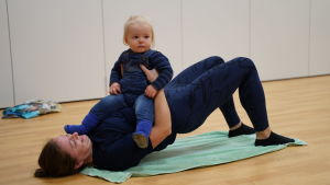 Mette Nyberg gympar med ett år gamla Edvin. En kvinna ligger på rygg med en bebis i famnen.