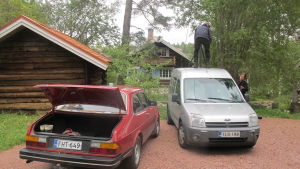 Inspelning av Stugor pågår. Två bilar står parkerade under en inspelning av Stugor. En fotograf står på den ena bilens tak.
