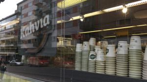De besvikna företagarna berättar att kunder som köper kaffe och andra lönsamma varor vänder om då de ser postkön. Bilden är arrangerad Engångskoppar står uppradade på en hylla. En skylt med texten kaffe hänger bredvid.