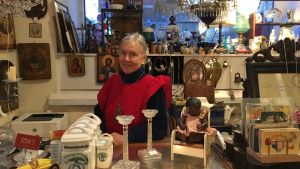 Ritva Blomqvist har klätt upp sig i en röd Marimekko-klänning inför julen. Ritva Blomqvist står i sin antikaffär iklädd en röd klänning.