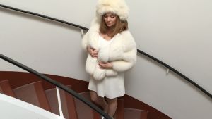 Emma Sandström klädd i en outfit a´la Catherine Deneuve på väg till studion. Emma Sandström står i en trappa i klädd vit pälsmössa, vit päls och klänning.
