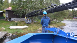 M/S Roope är försedd med en lyftkran med vars hjälp man behändigt får ombord båtarna som ska bort. Lyftanordning på väg att gripa tag om en gammal roddbåt.