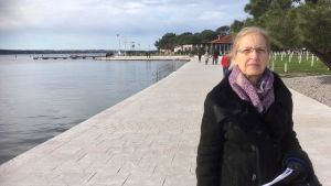 Duša Krnel Umek står på strandpromenaden i den slovenska badorten Portoroz. På andra sidan Piranbukten skymtar den idag kroatiska halvön Savudrija. Duša Krnel Umek, en slovensk etnolog och politiker.