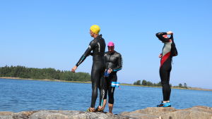 Nöjda efter träning. Tre män iklädda våtdräkter står på klippor i Kristinestads skärgård.