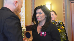 Tidningen Uusimaas chefredaktör Anne Lahnajärvi överräcker Runeberg-medaljen. En kvinna med mörkt hår ler och ger något åt en skallig man med skägg.