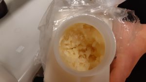 frusen björkolja gul frusen geggamoja i plastburk i plastpåse. en hand håller burken