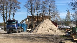 Här ska byggas nytt. Ett större fordon vid ett halvrivet hus och en stor sandhög.